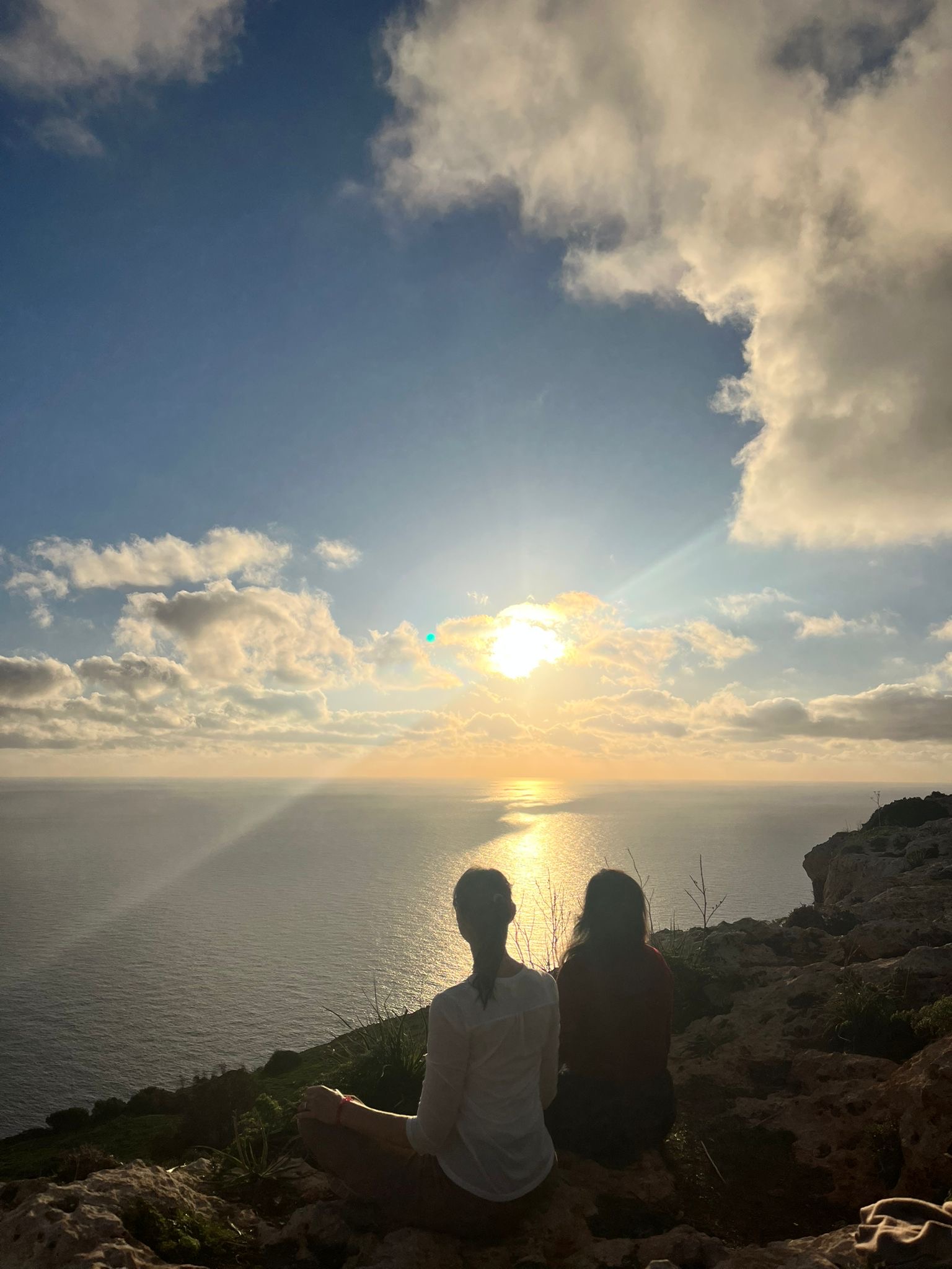 Zwei Personen meditieren im Sitzen bei Sonnenuntergang am Meer